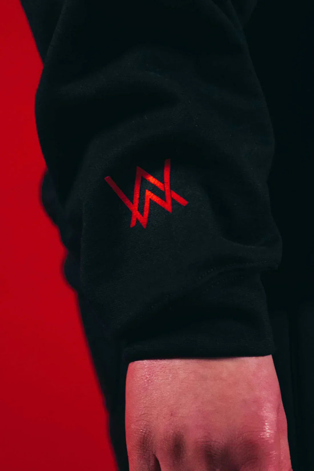 Detailed image of the Alan Walker Fake a Smile Hoodie's sleeve, featuring the distinctive red Alan Walker logo against the black fabric.