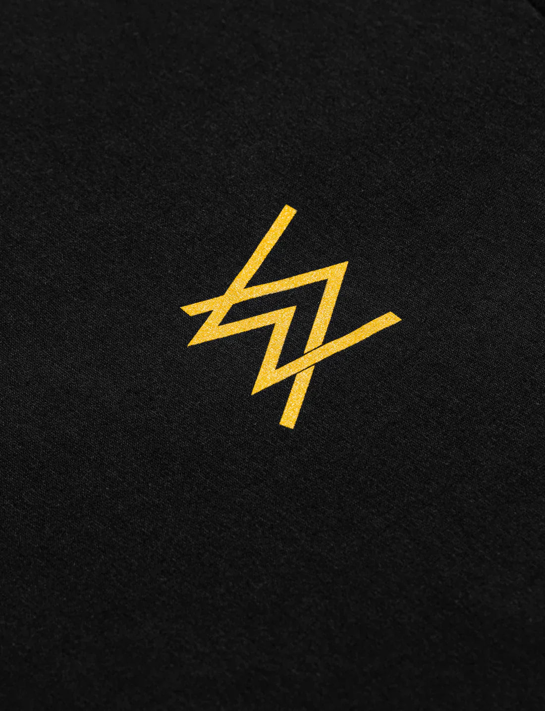 Close-up of a golden-colored Alan Walker logo printed on a black t-shirt.