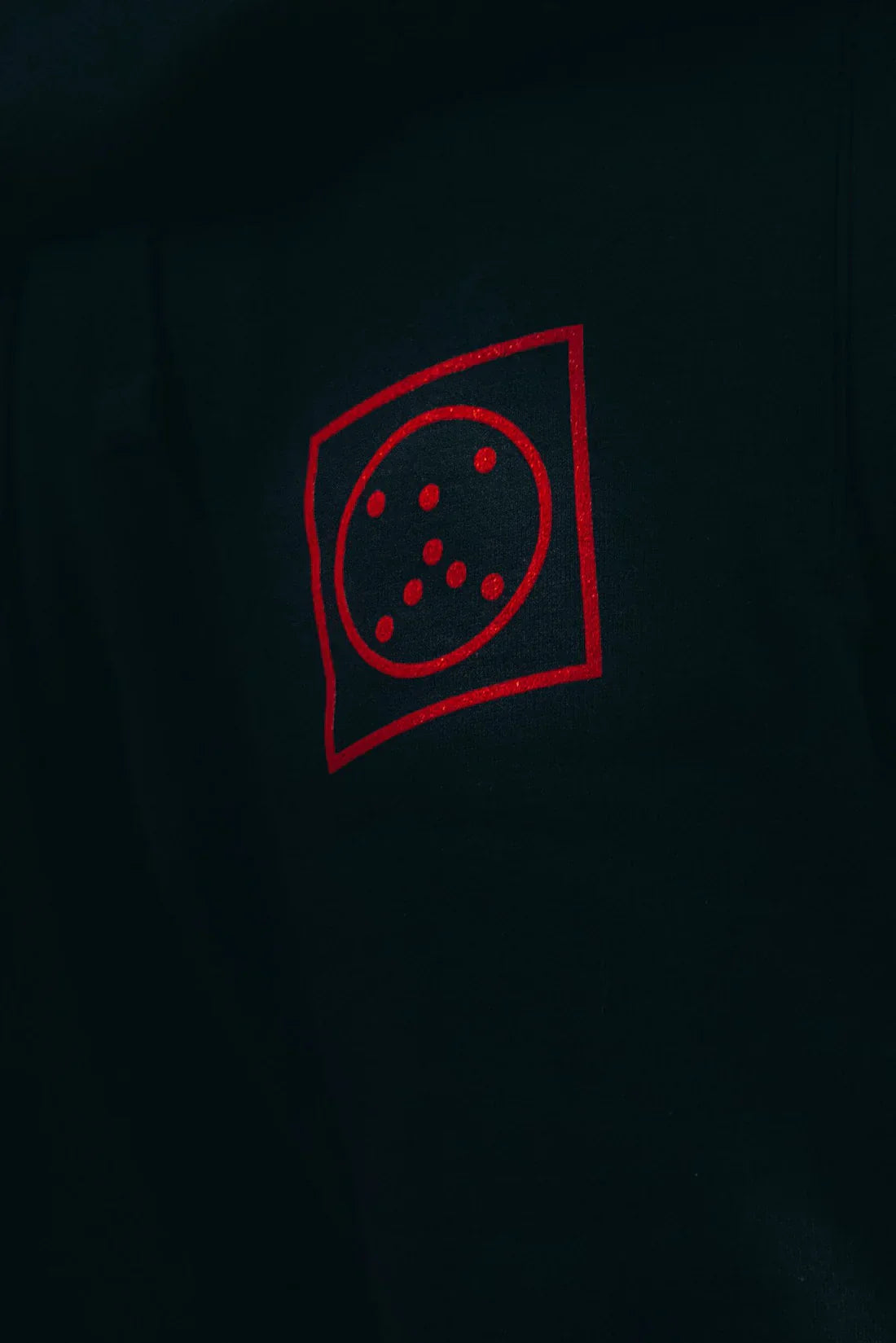 Close-up of a detail on black sweatpants, showcasing a red Alan Walker branded graphic icon.