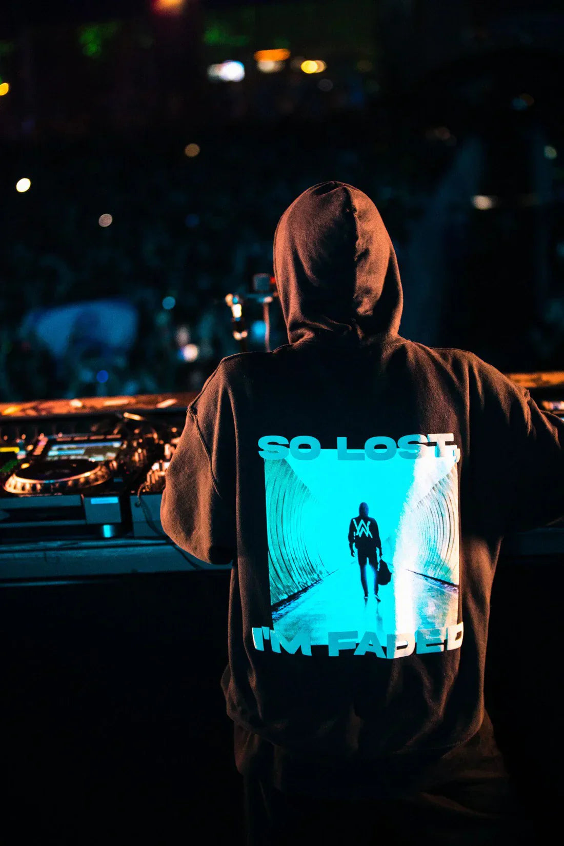 DJ facing a vibrant crowd with back turned to the camera, wearing Alan Walker's Faded hoodie with the illuminated text 'SO LOST I'M FADED' and a figure walking into light, capturing the essence of live electronic music performances.