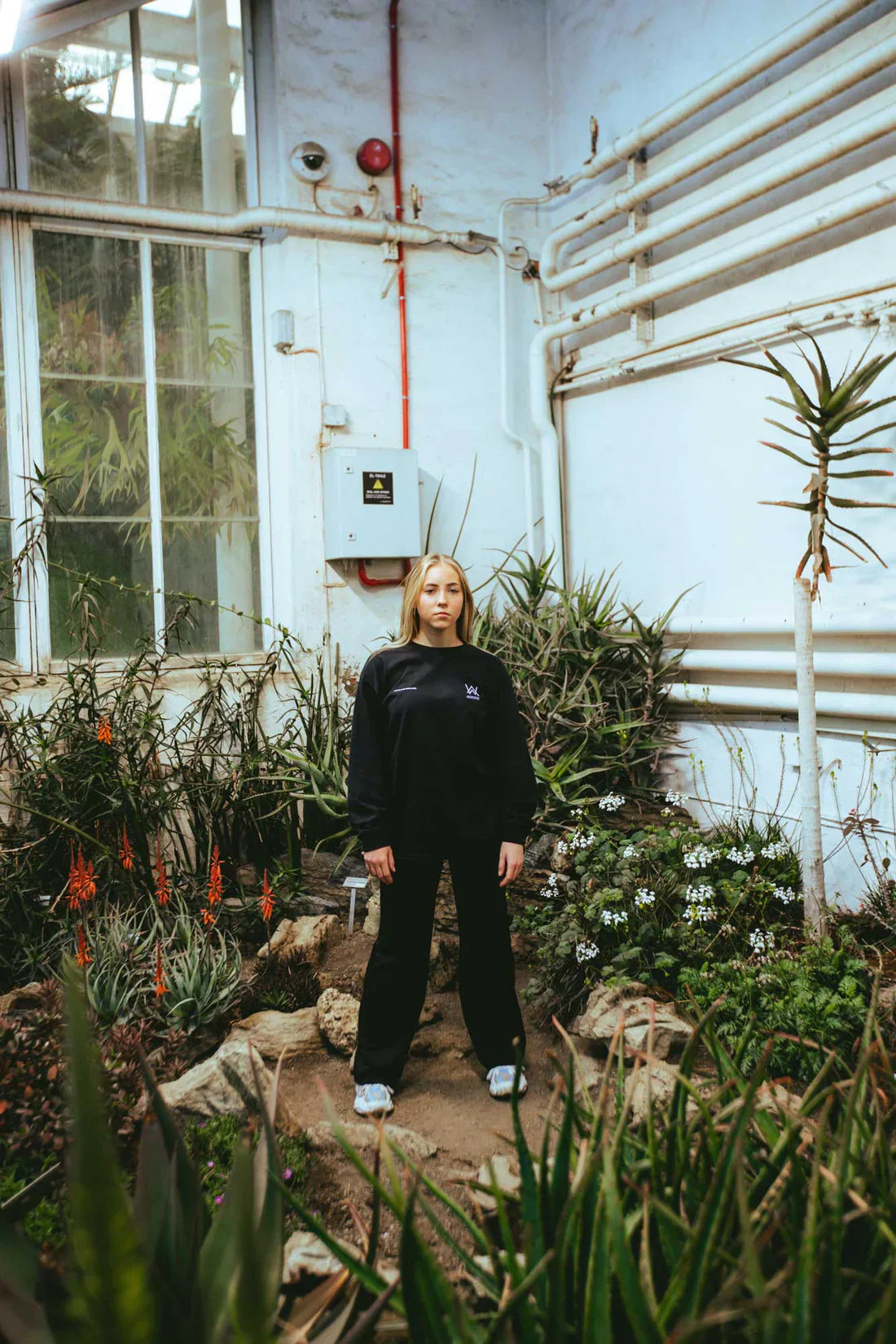 Female model striking a relaxed pose in the Melting Rose Longsleeve, perfectly complementing the natural greenhouse surroundings.