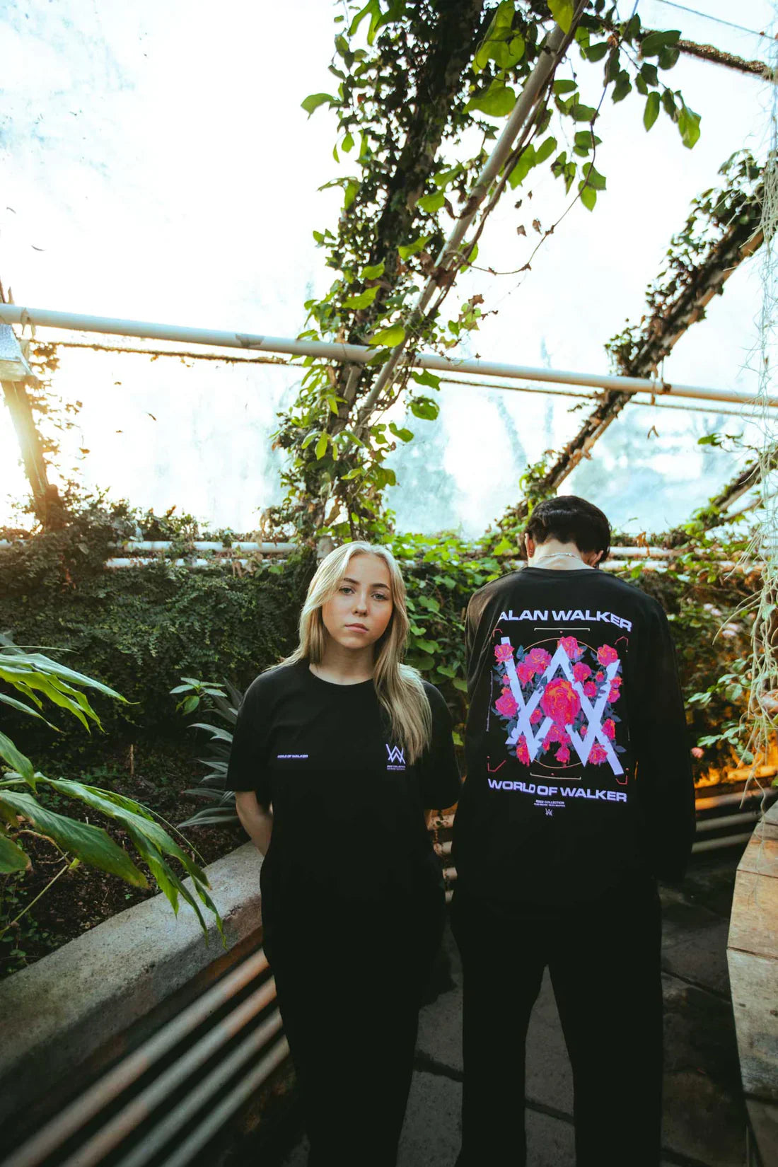 Couple in Melting Rose T-shirts presenting a front-and-back view, immersed in the serene ambiance of a greenhouse.