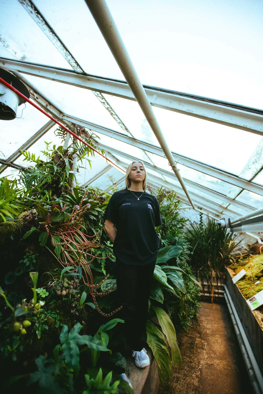 Female model casually poses in the black Melting Rose T-shirt inside a botanical conservatory, exuding relaxed vibes.