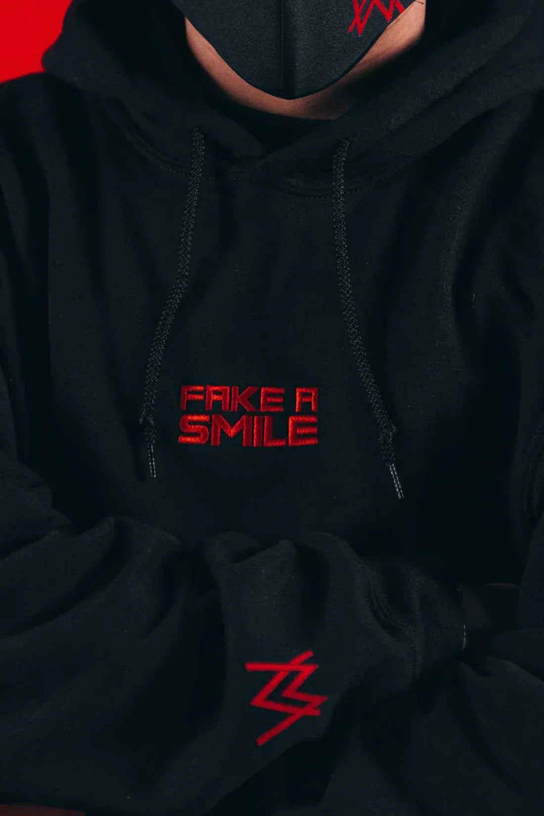 Close-up of the Alan Walker Fake a Smile Hoodie showing detailed red glitched text of 'FAKE A SMILE' with the iconic Alan Walker logo beneath.