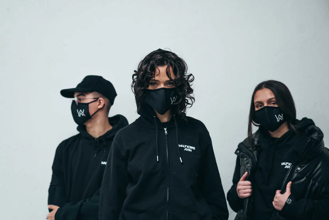 Trio wearing Alan Walker's CORE LOGO ZIP HOODIE and face masks, each emblazoned with the AW logo, standing confidently against a minimalist backdrop, representing unity in style and urban fashion.