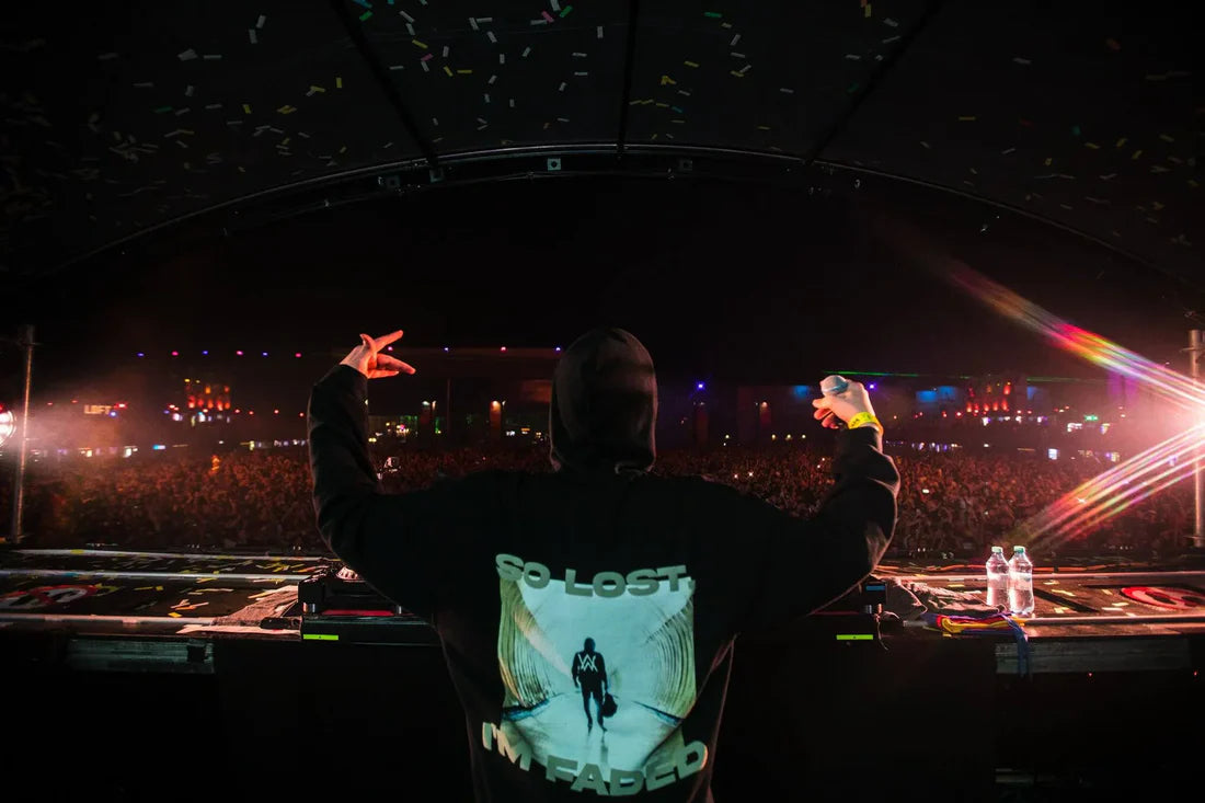 Energetic DJ on stage at a music festival, gesturing a peace sign while wearing Alan Walker's Faded hoodie, backlit by stage lights with a captivated crowd in the foreground.