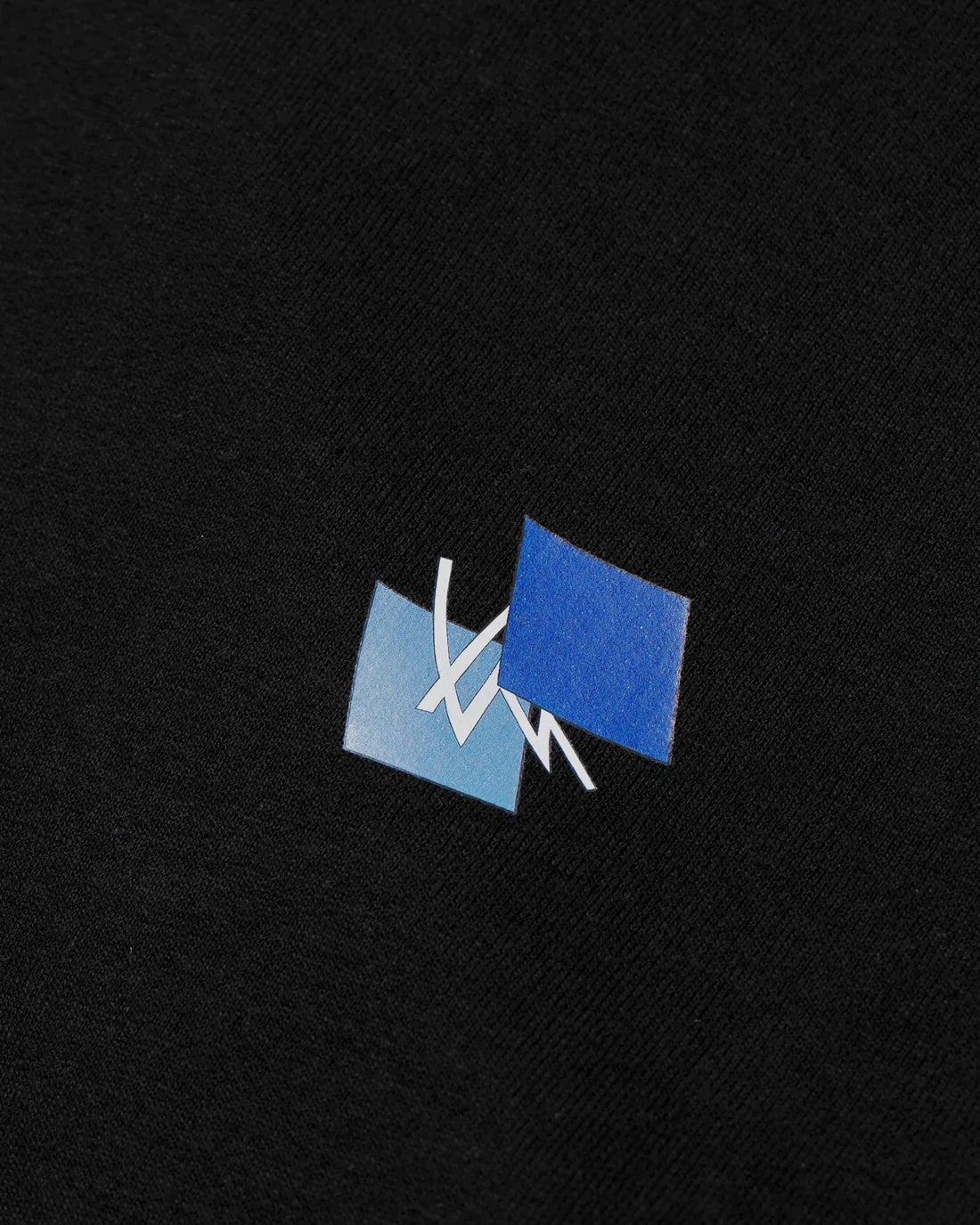 Close-up of the Alan Walker Blueprint T-Shirt's blue logo patch on the black fabric, showcasing the brand's iconic symbol in high contrast.